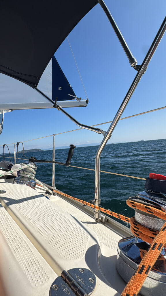 The deck of a sailing boat under way; an orange sheet on the winch, the coastline and islands in the distance.