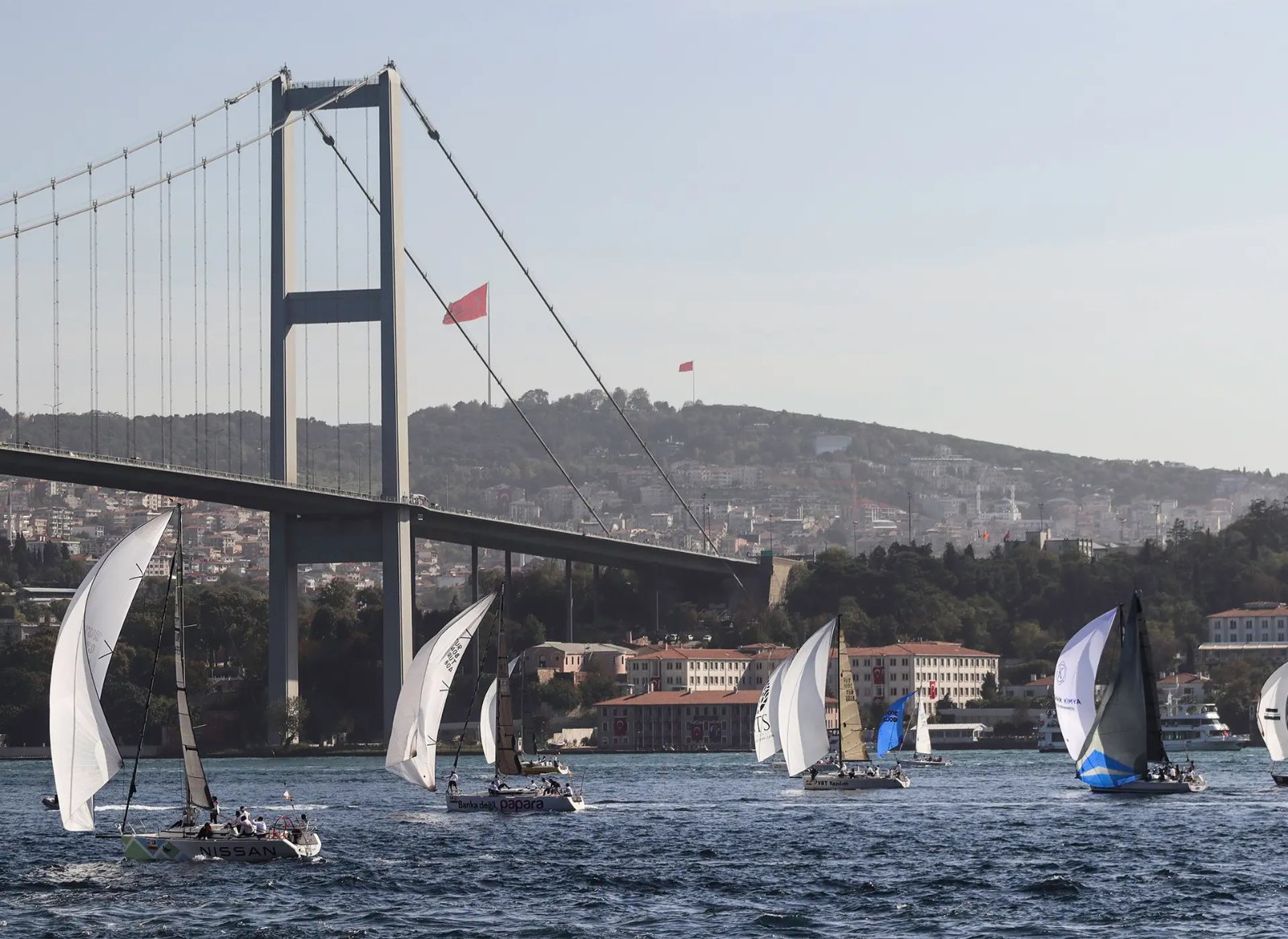 Boğaz Köprüsü altında yelken sponsorluğu logoları taşıyan yarış tekneleri