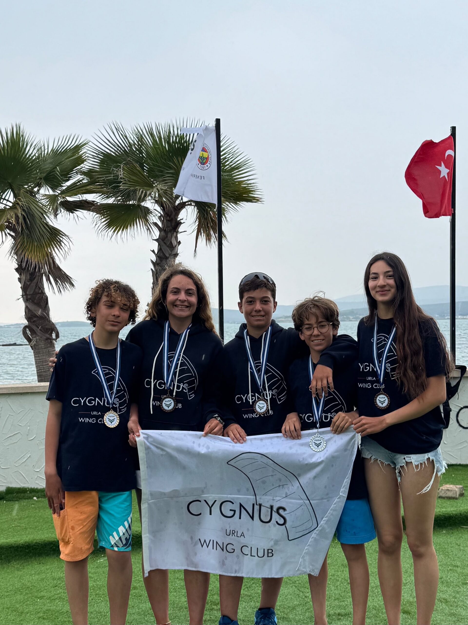Cygnus Urla Wing Club sporcuları madalyaları ve kulüp bayrağıyla